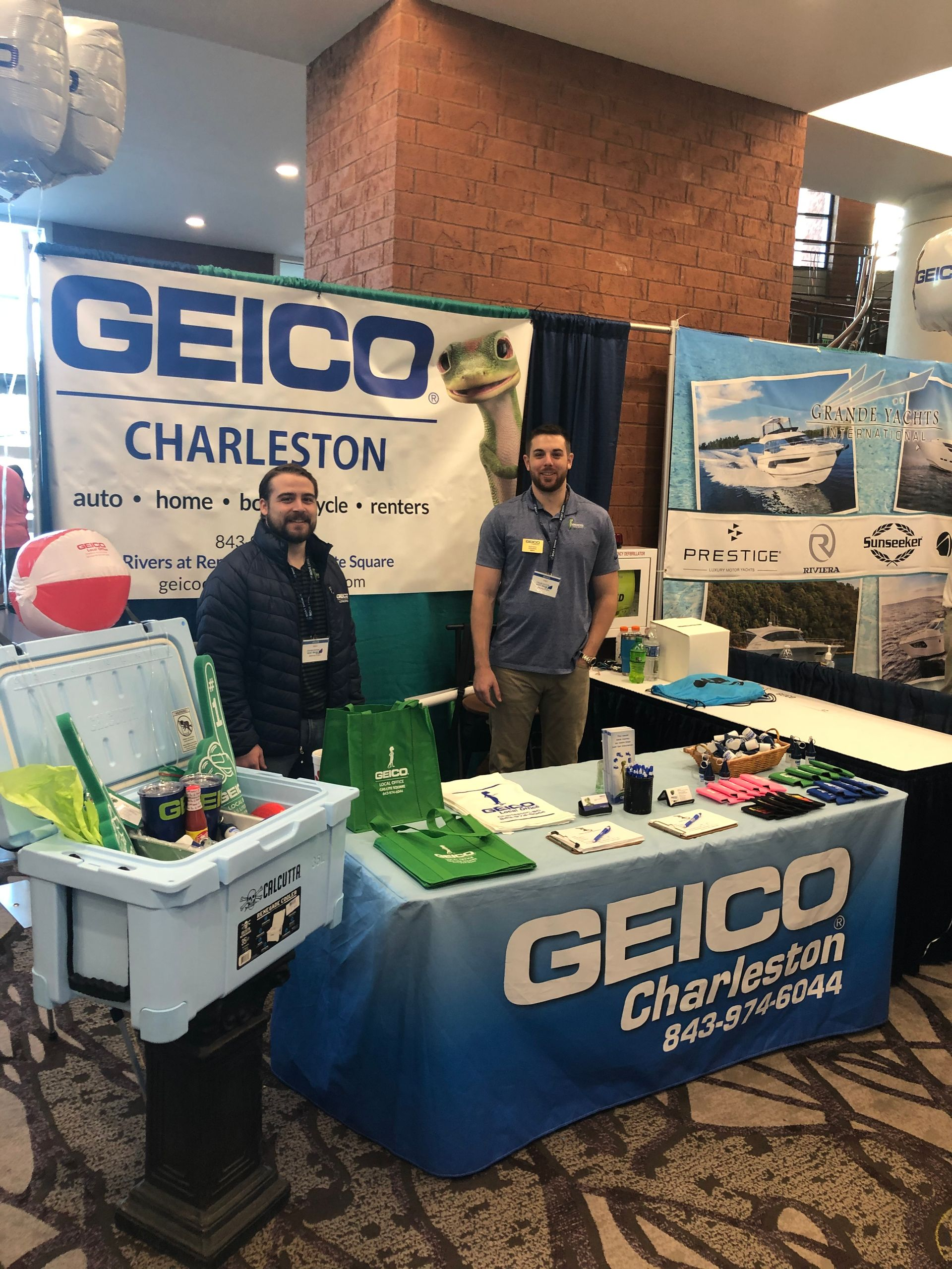Two men at a GEICO Charleston booth. Banner behind them with their logo and a turtle mascot.