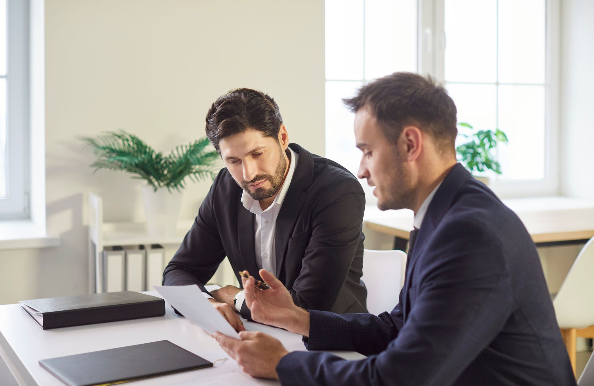 Two men in suits reviewing documents at a table.