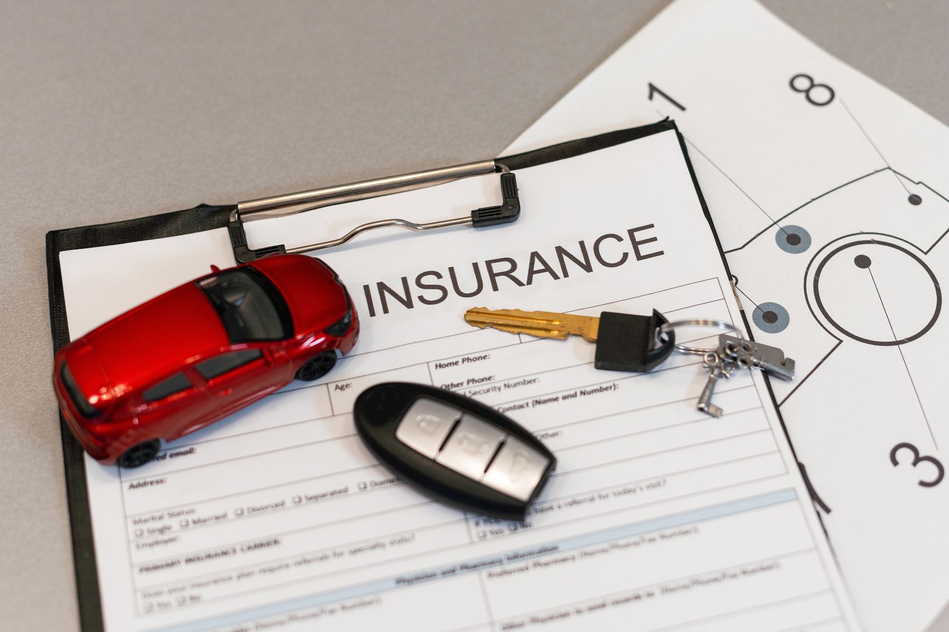 Red toy car, car keys, and key fob on an insurance document.