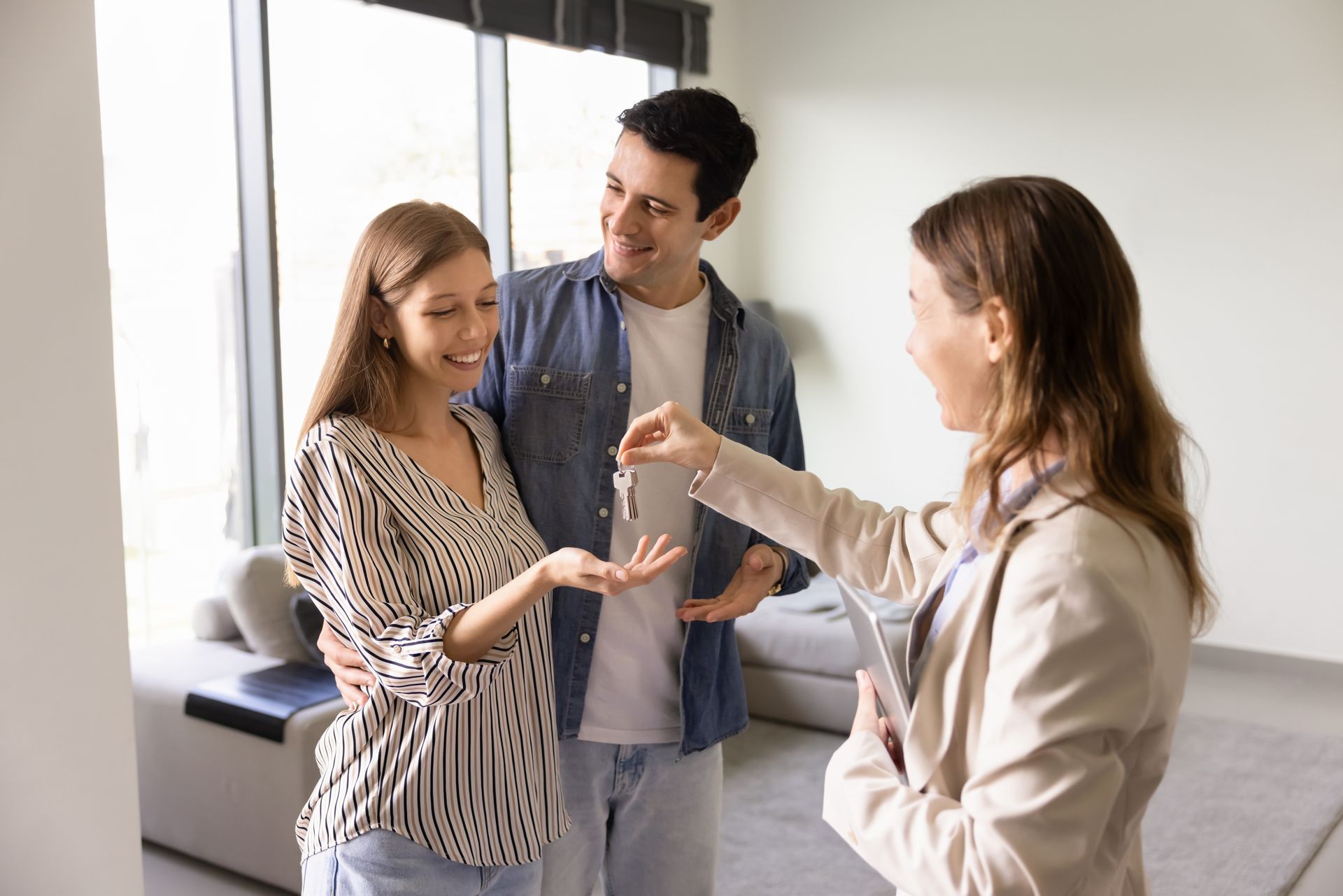 Real estate agent handing keys to a smiling couple in a bright, modern room.