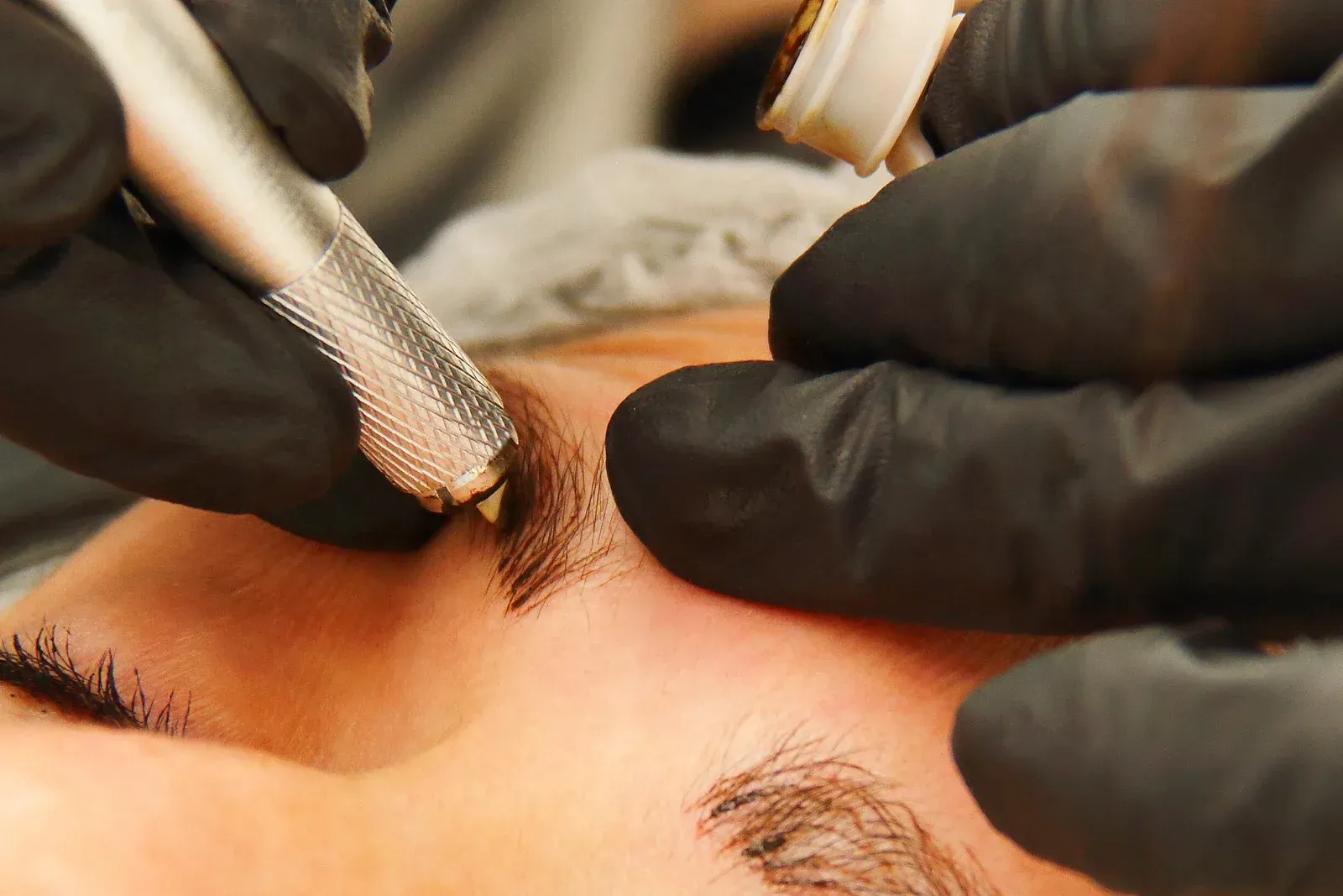 A person is getting a permanent makeup tattoo on their eyebrows.