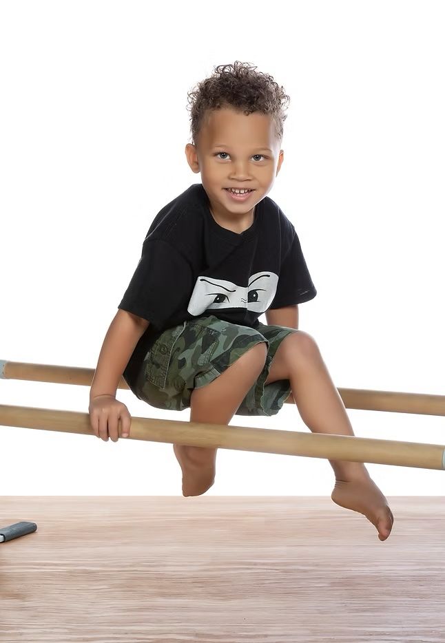 A young boy in a white shirt is flexing his muscles.