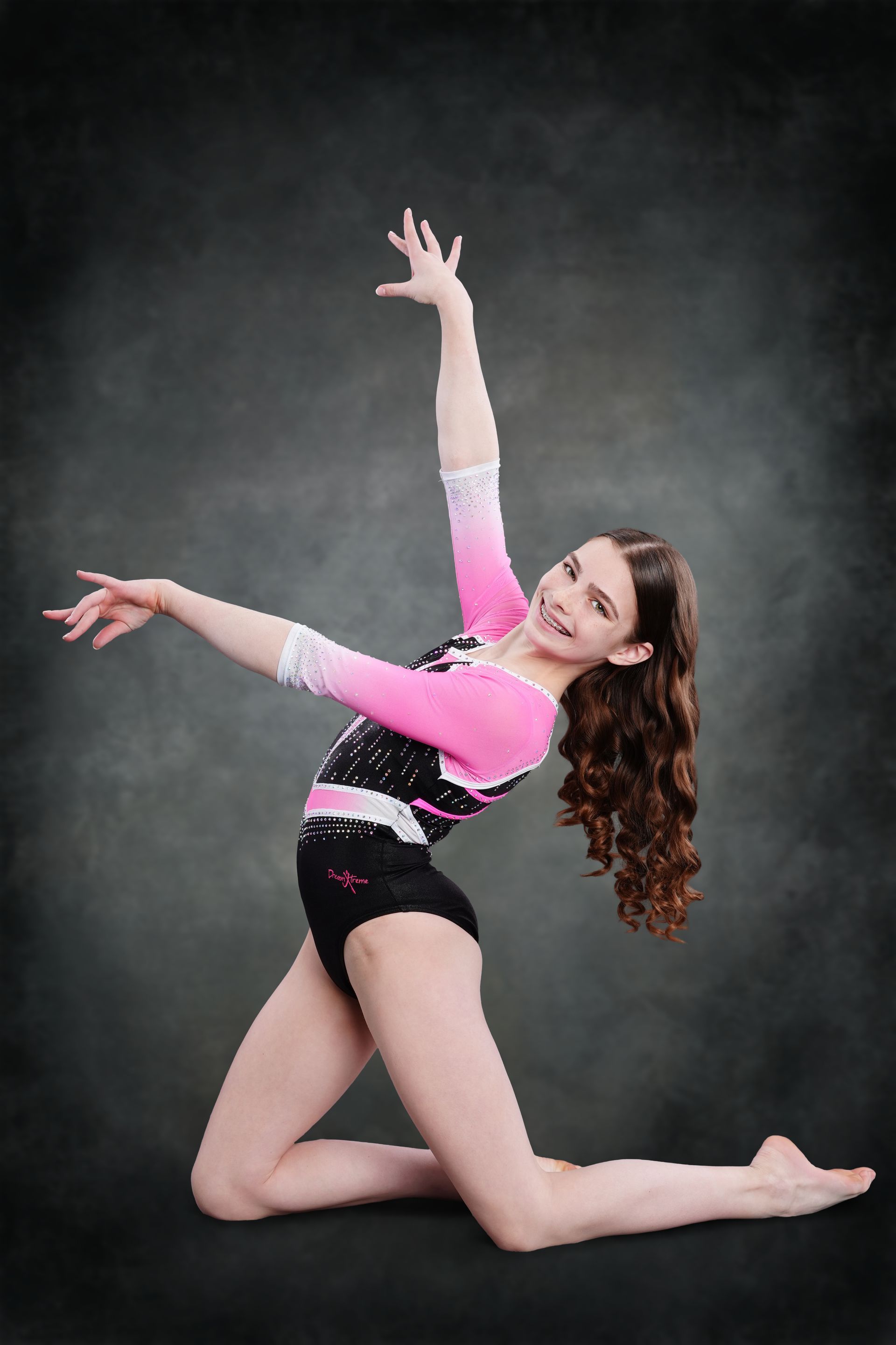 A female gymnast is posing for a picture in front of a pink background.