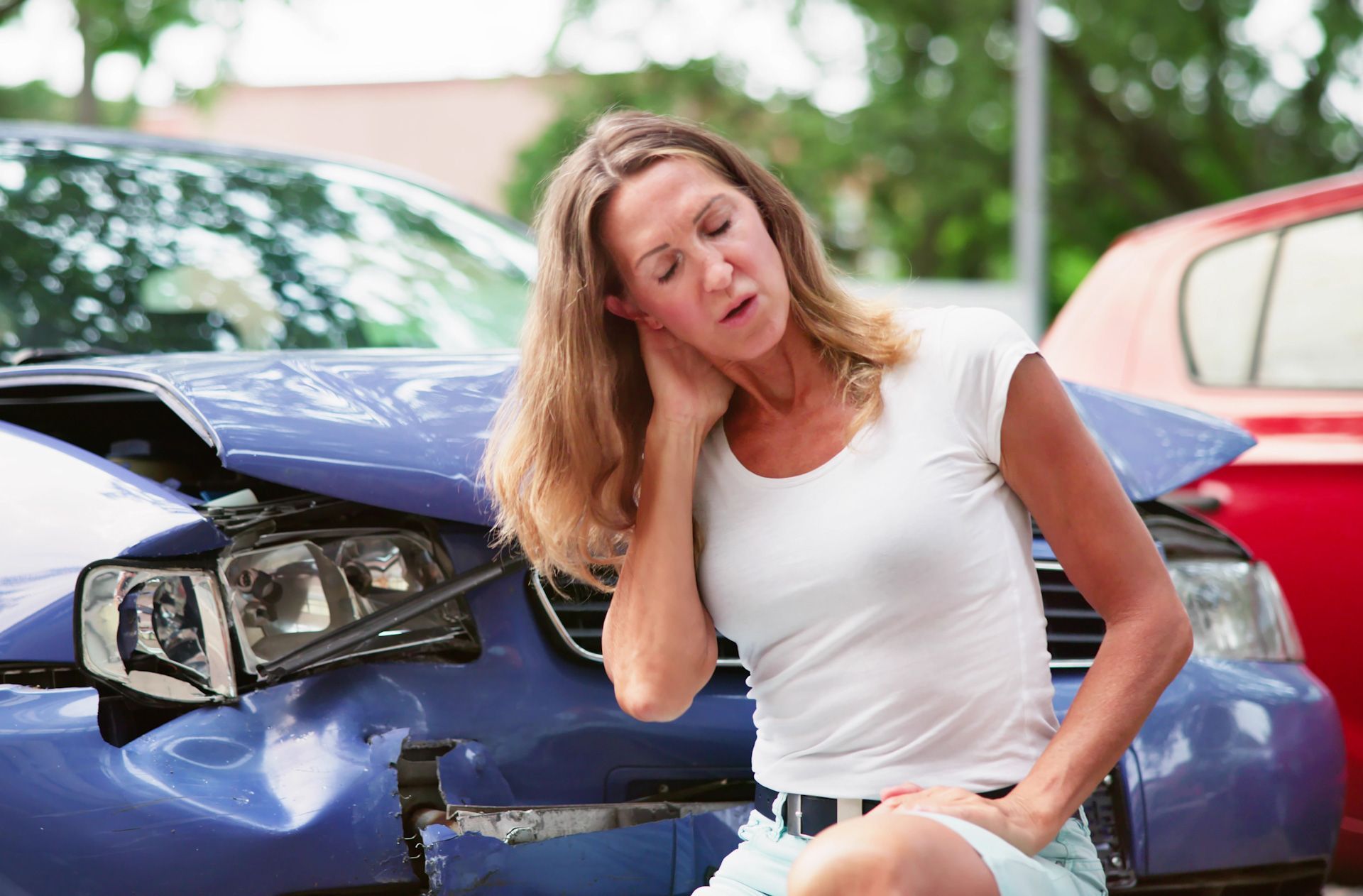 A woman is sitting in front of a damaged car