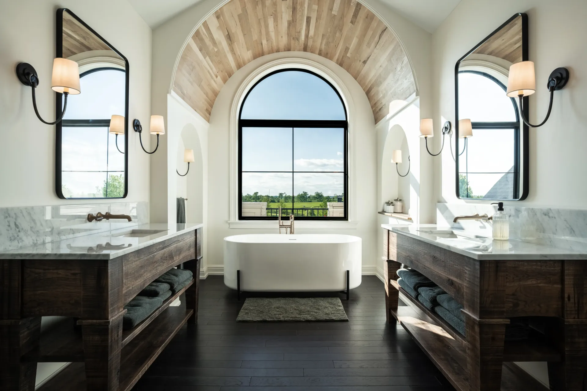 Spacious bathroom with wood accents, large arched window, two vanities, and a central soaking tub.