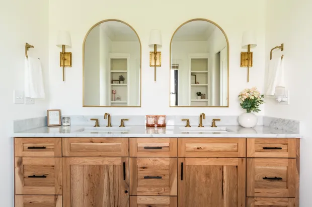 Bathroom with wooden vanity, marble countertop, gold arched mirrors, and sconces.
