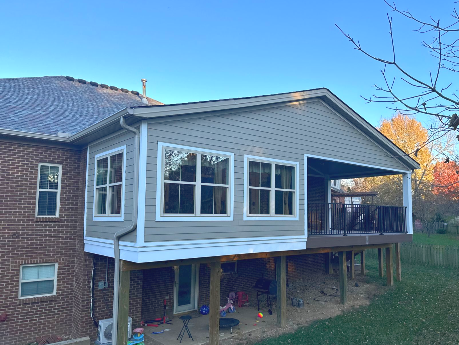 A house with a deck and enclosed sunroom, brown siding, and white trim. Blue sky.