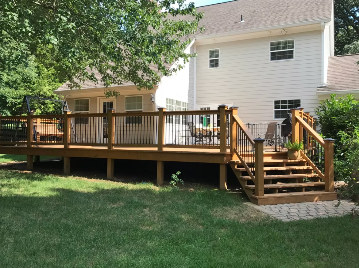 Backyard deck with stairs leading to a white house; brown deck boards and railing, green lawn.