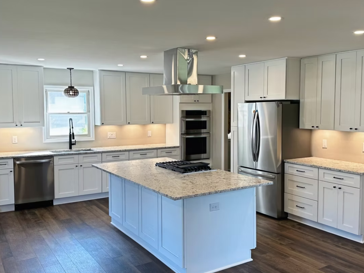 Modern white kitchen with stainless steel appliances, granite island, and dark wood floors.