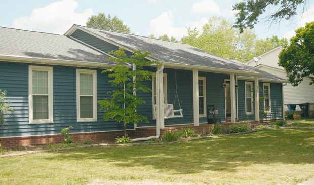 Blue house with white trim, porch swing, and green lawn.