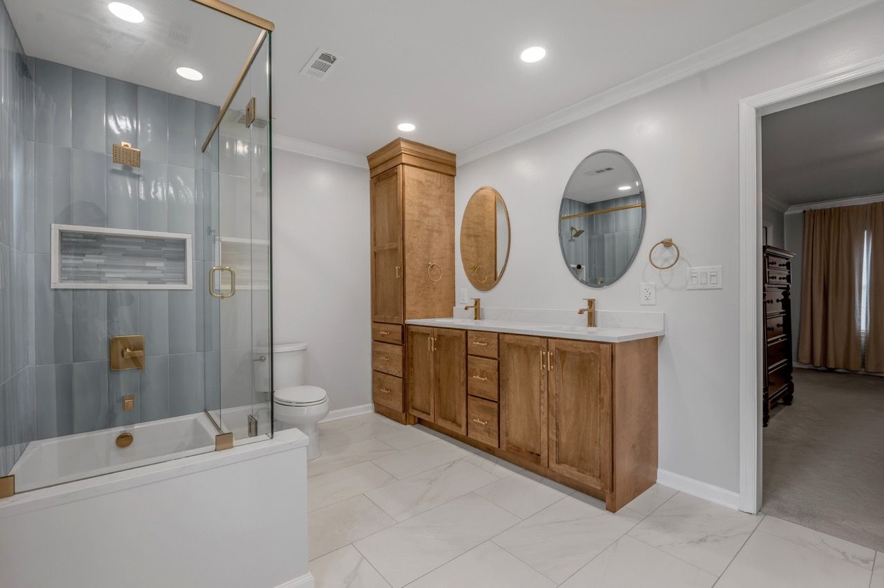 Modern bathroom with light blue shower tiles, wood vanity, and gold fixtures.