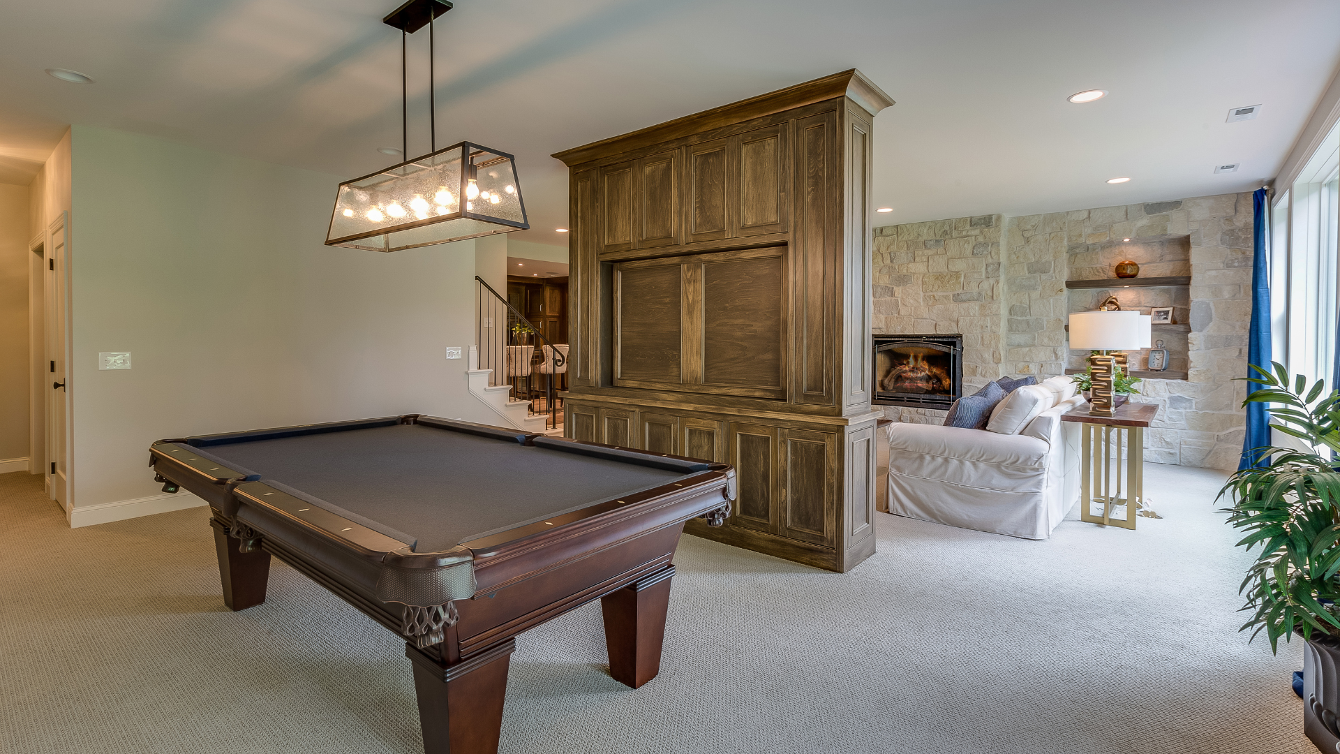 Pool table in a game room with stone fireplace, TV cabinet, and seating.