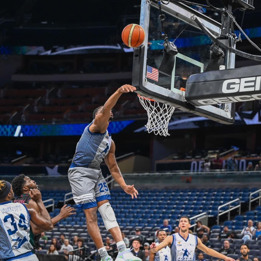 A basketball player is jumping in the air to catch a basketball in the net.
