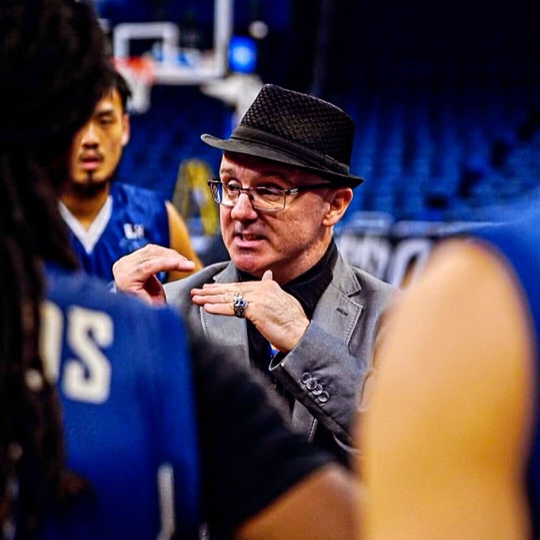 A man in a suit and hat is talking to a group of basketball players.