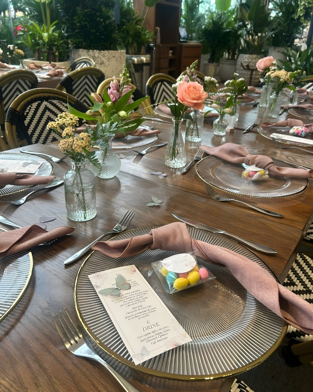 Juego de mesa y sillas para exteriores con platos a rayas, servilletas rosas, flores y coloridos macarons.