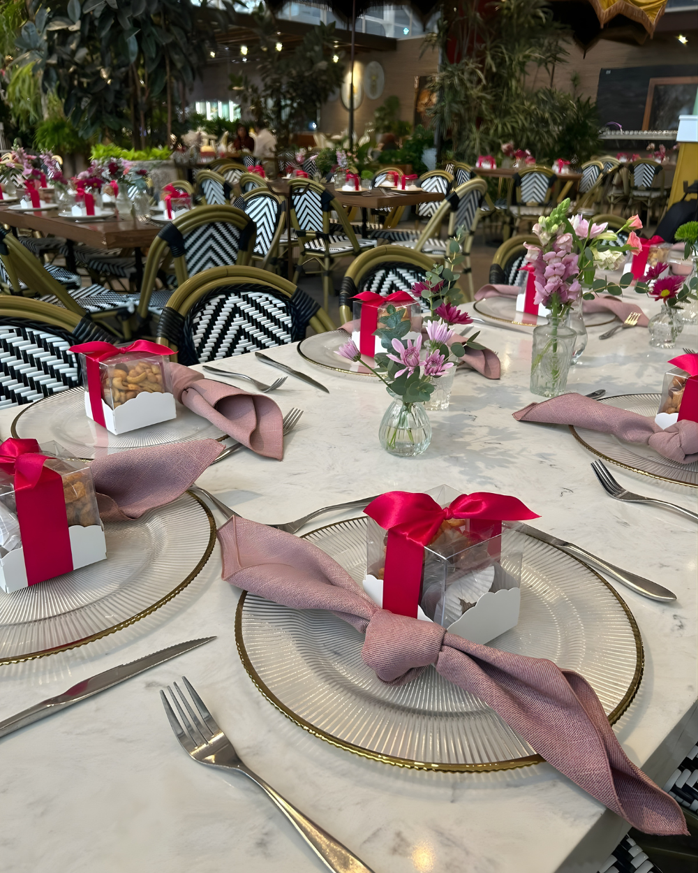Elegantes mesas de banquete, decoradas con flores rosas, bajoplatos dorados y servilletas malva bajo una iluminación festiva.