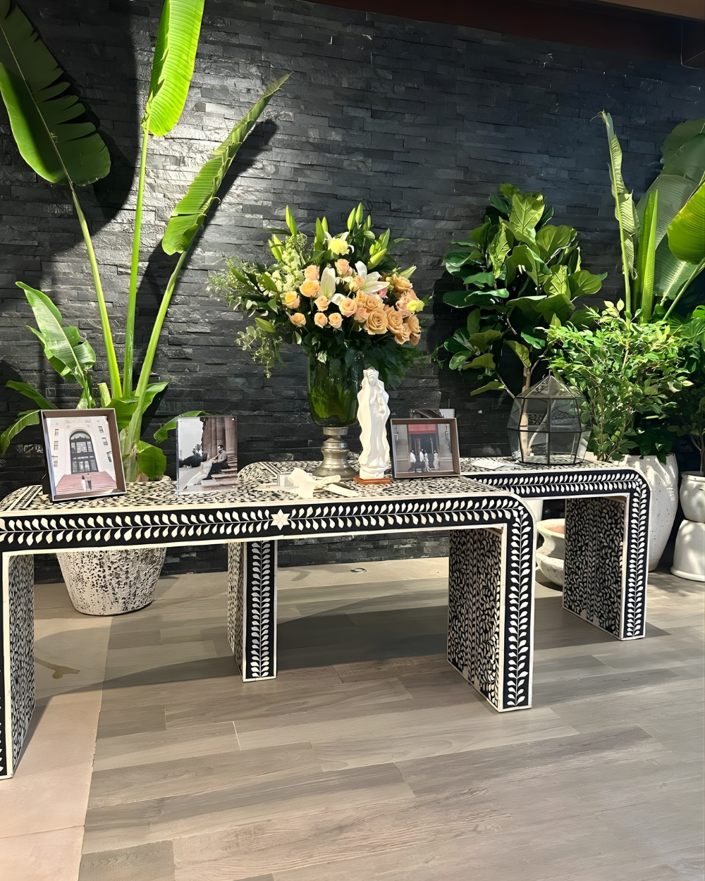 Mesa conmemorativa decorada con fotos enmarcadas, velas, flores y una estatua blanca sobre una pared negra.
