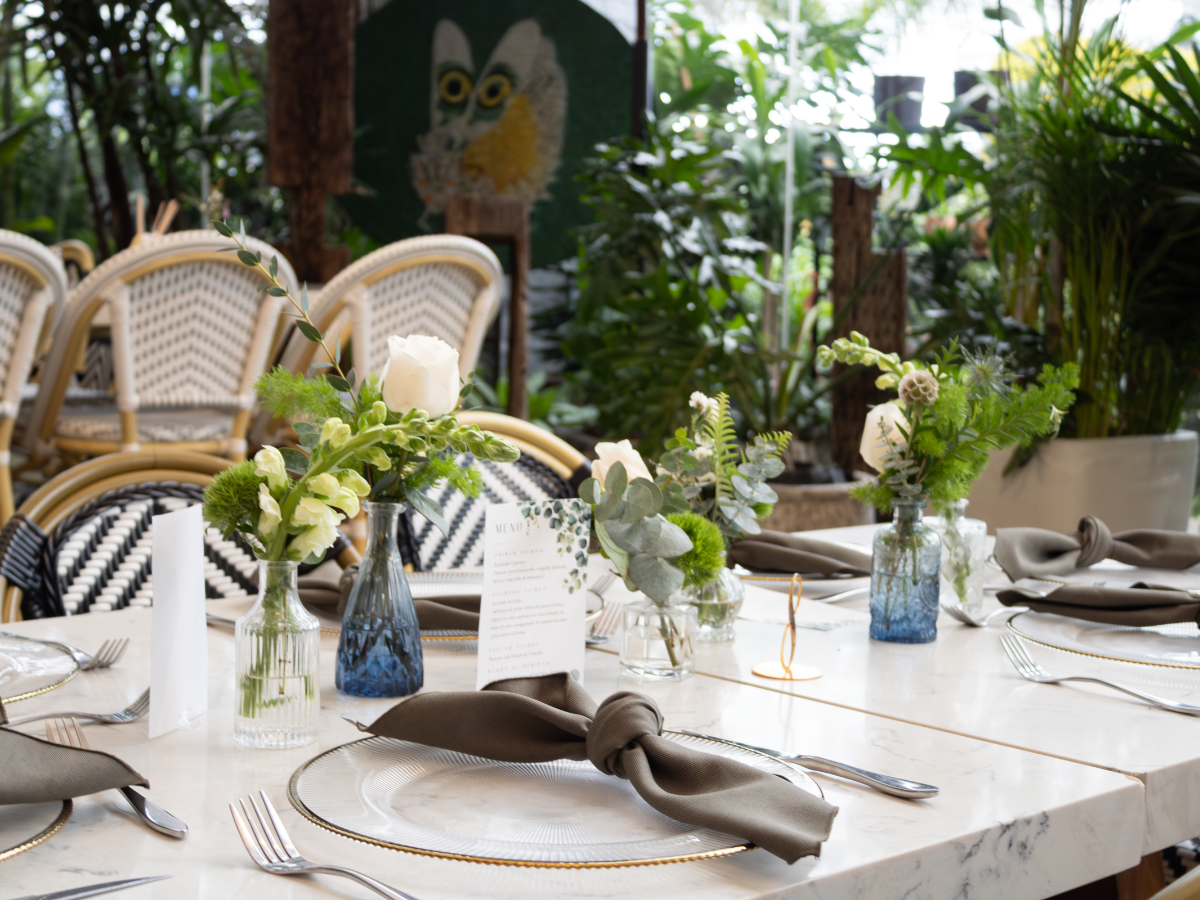 Elegante conjunto de mesa y sillas blancas para comer, centros de mesa florales y servilletas en un entorno ajardinado.