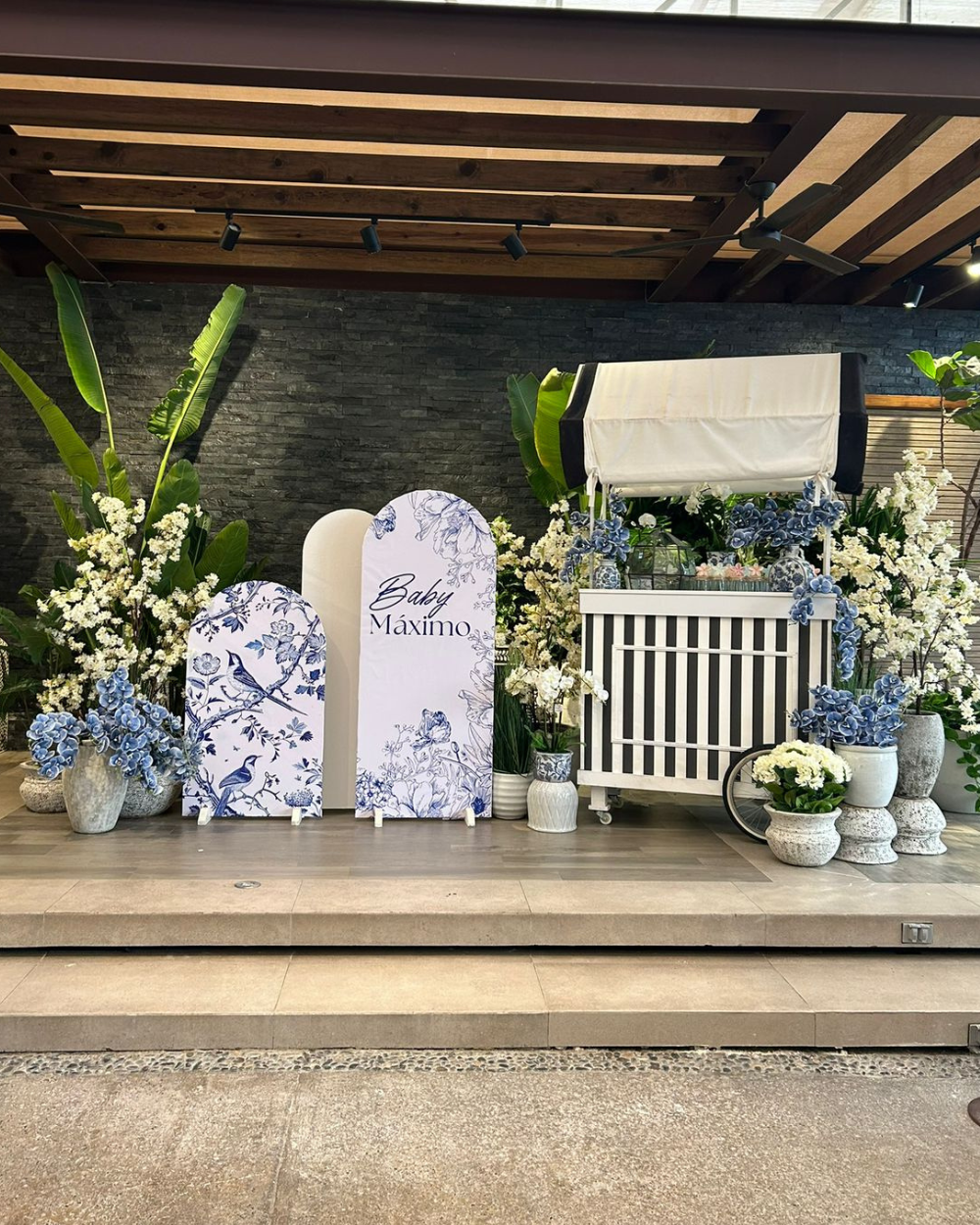 Exhibición floral conmemorativa en azul y blanco con marcadores arqueados, flores y velas en un escenario en el porche.