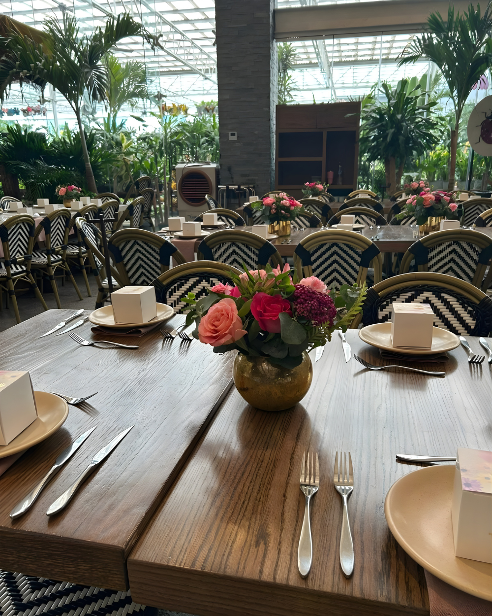 Mesa decorada con flores en un luminoso restaurante con invernadero y cubiertos vacíos.