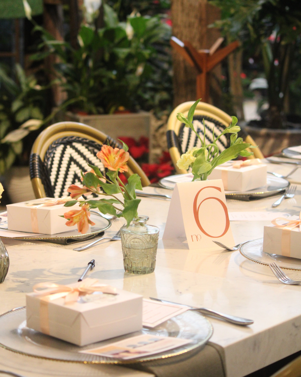 Elegante mesa puesta con vajilla blanca, centros de mesa florales y sillas estampadas en un restaurante.
