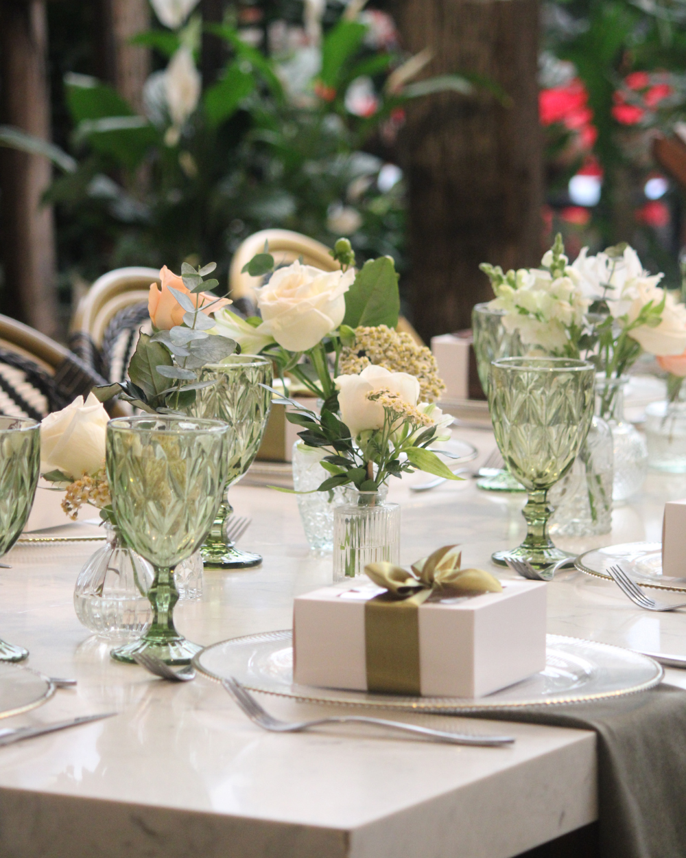 Elegante mesa de exterior decorada con rosas blancas, copas de cristal y cajas de regalo envueltas.