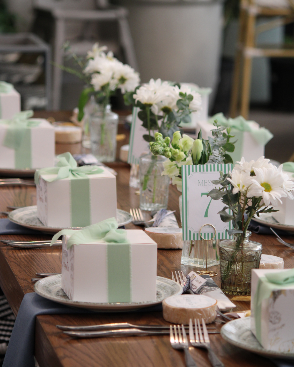 Cajas de regalo en tonos pastel con flores blancas dispuestas sobre una mesa de comedor puesta.