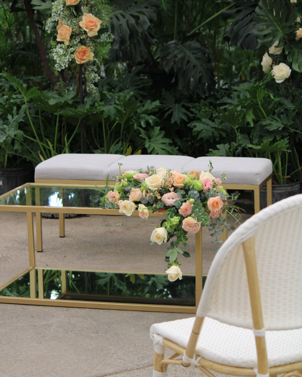 Mesa y banco dorados decorados con flores en un jardín tropical, con una silla blanca en primer plano.