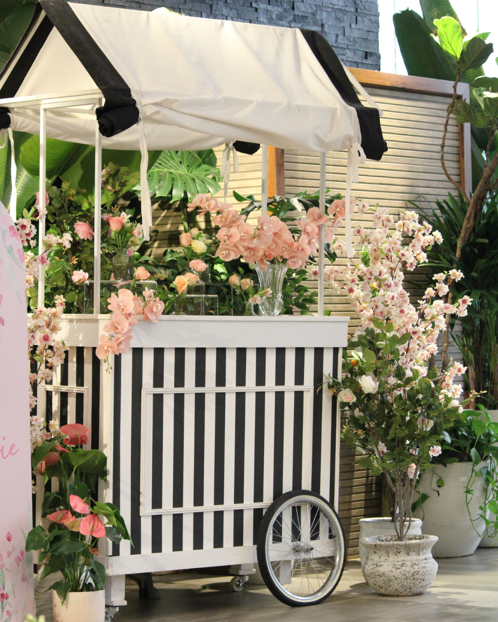 Carrito blanco y negro decorado con flores rosas en un patio ajardinado.