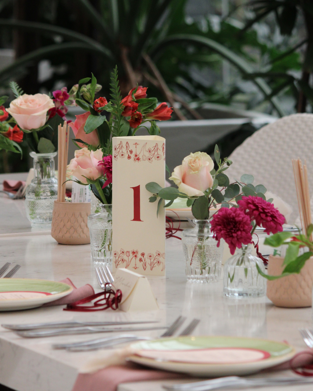 Decoración floral de mesa con rosas, flores rojas y una tarjeta con el número de mesa en una mesa de evento al aire libre.