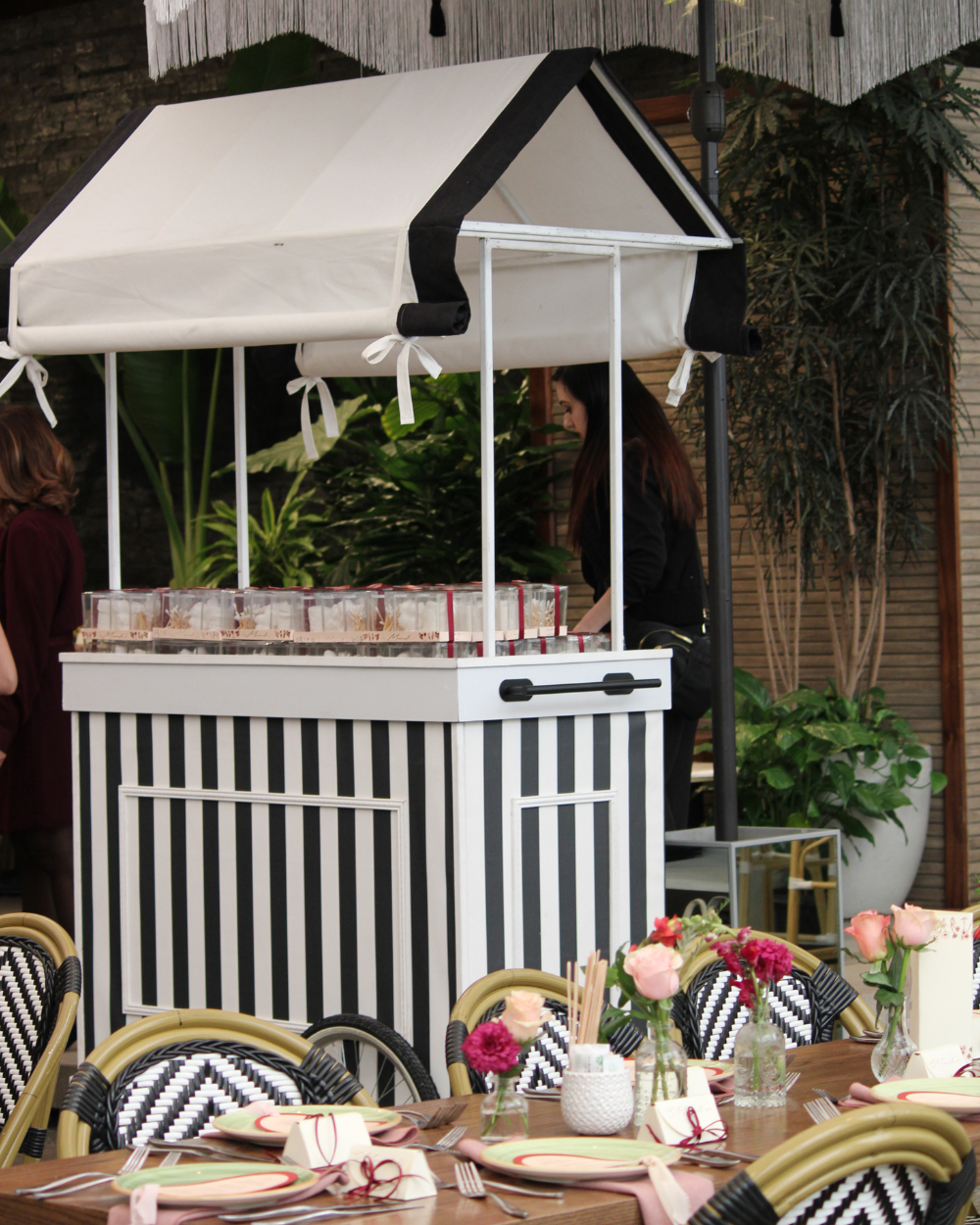 Carrito a rayas blancas y negras con toldo y flores en una mesa de eventos al aire libre
