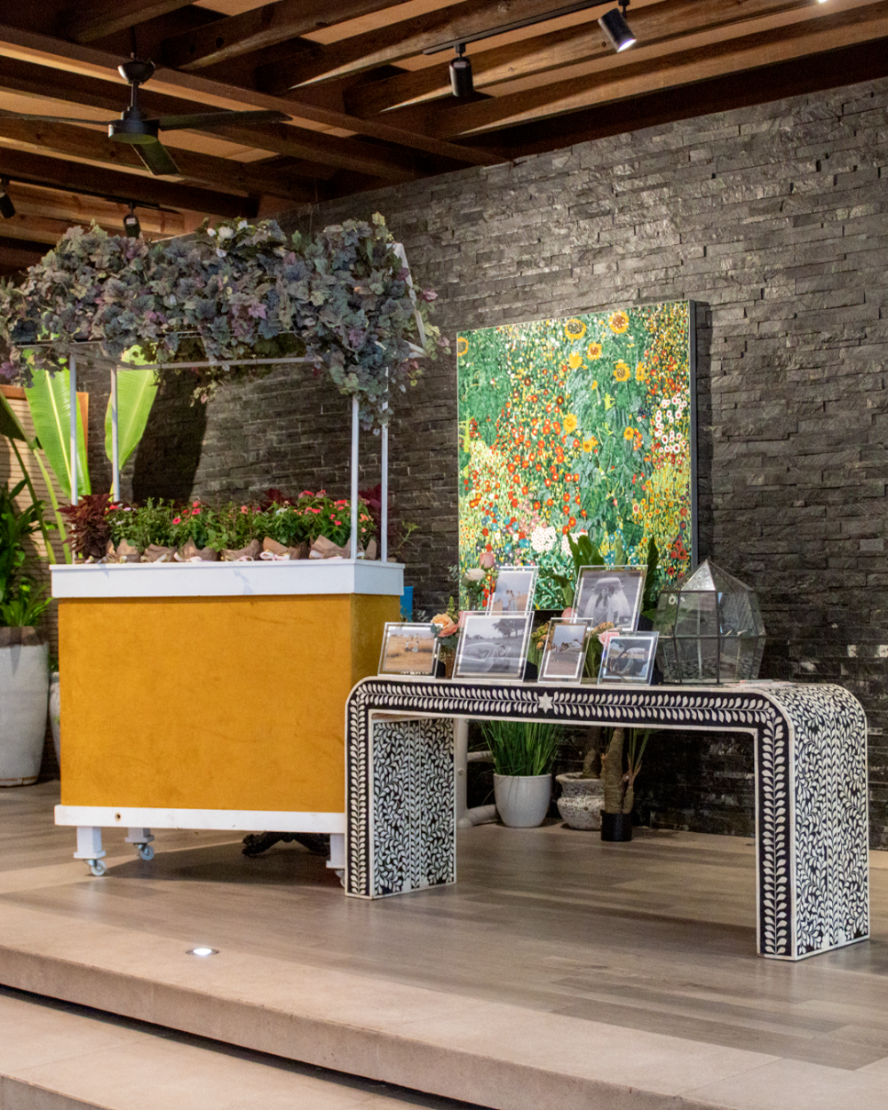 Arreglo floral de interior con una maceta amarilla, pared de piedra y mesa consola estampada.