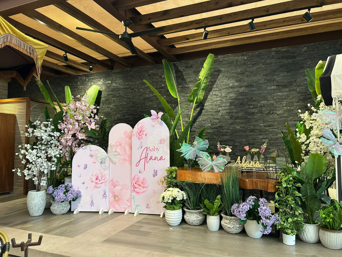 Fondo para eventos con motivos florales en tonos pastel, paneles blancos, arreglos florales y plantas en macetas.