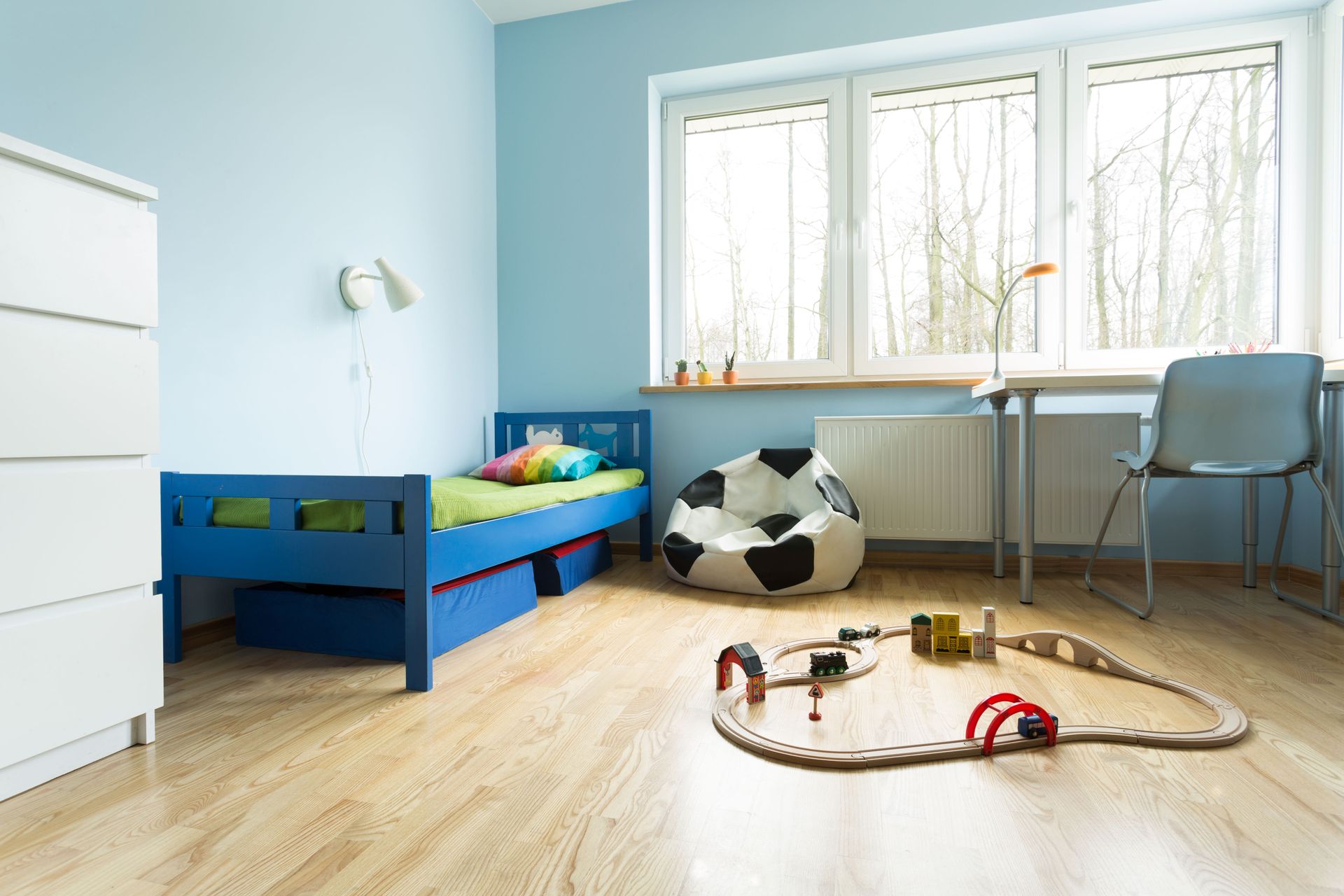 Luminosa camera da letto per bambini con un letto blu, una scrivania vicino alla finestra