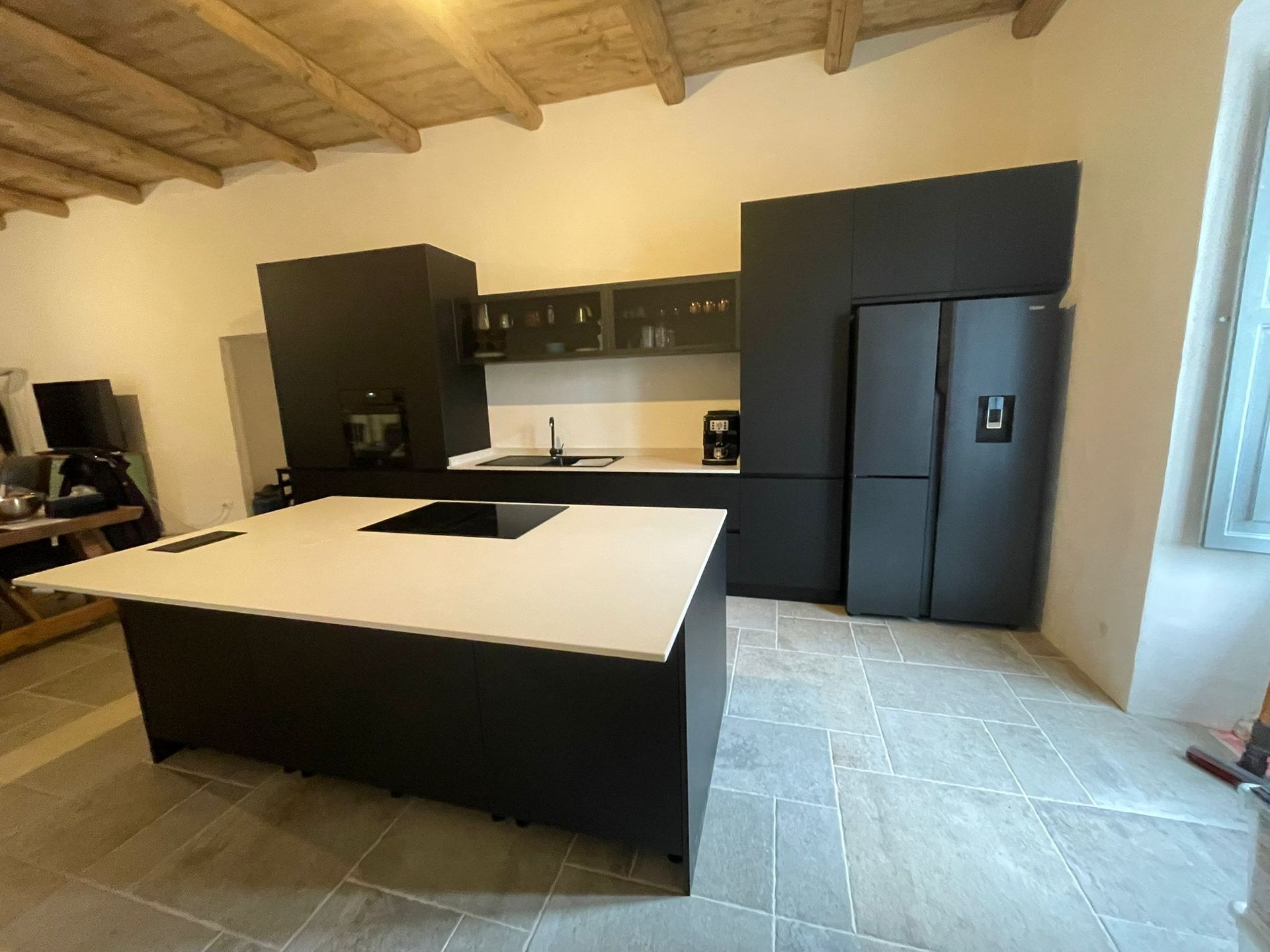 Cucina moderna con mobili scuri, isola bianca e pavimento piastrellato sotto un soffitto con travi in legno