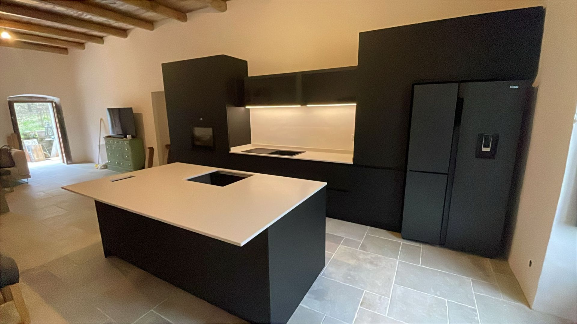Cucina moderna con mobili neri, piani di lavoro bianchi, isola centrale e frigorifero in acciaio inox