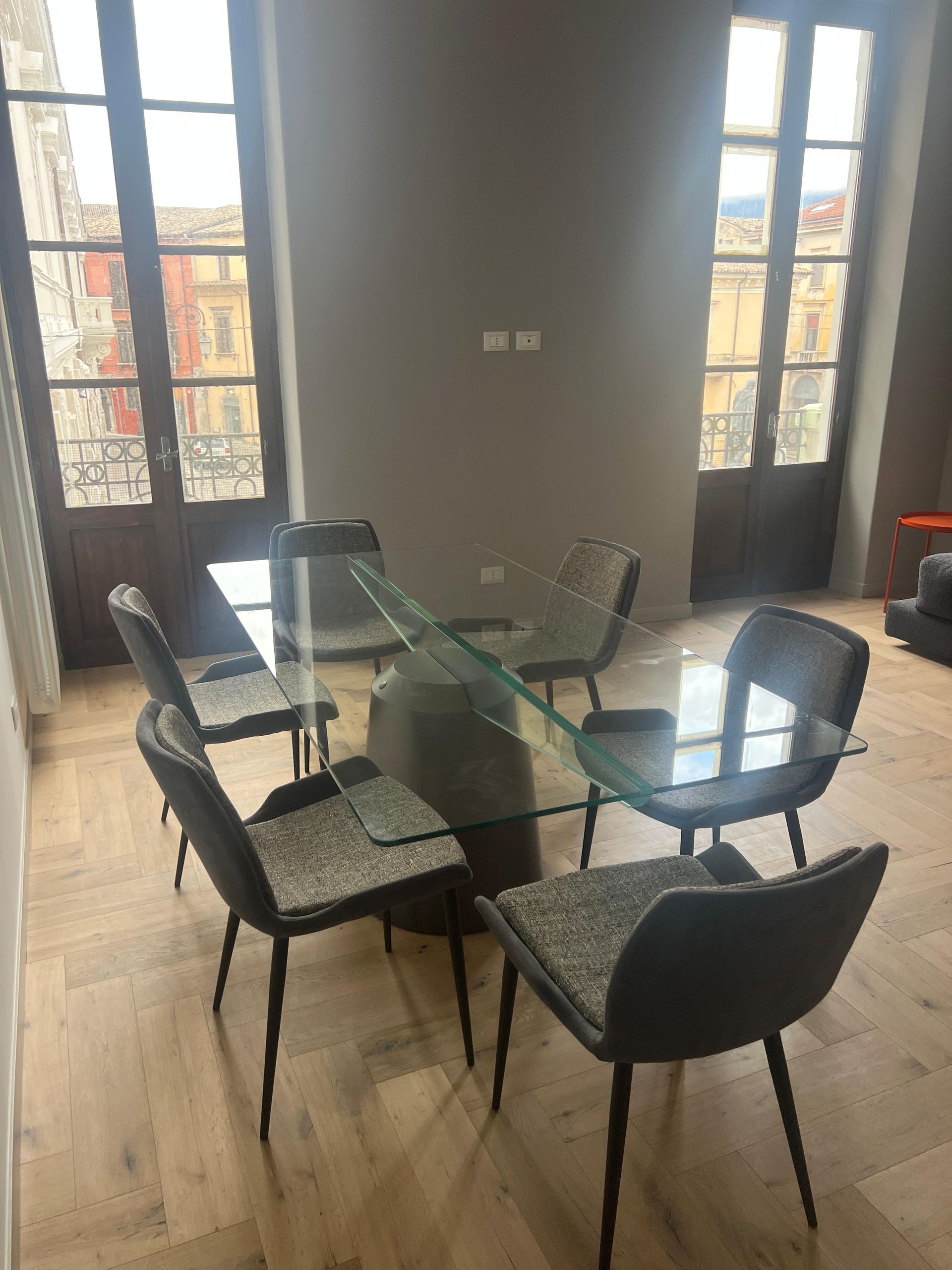 Sala da pranzo moderna con tavolo in vetro e quattro sedie nere vicino a grandi finestre