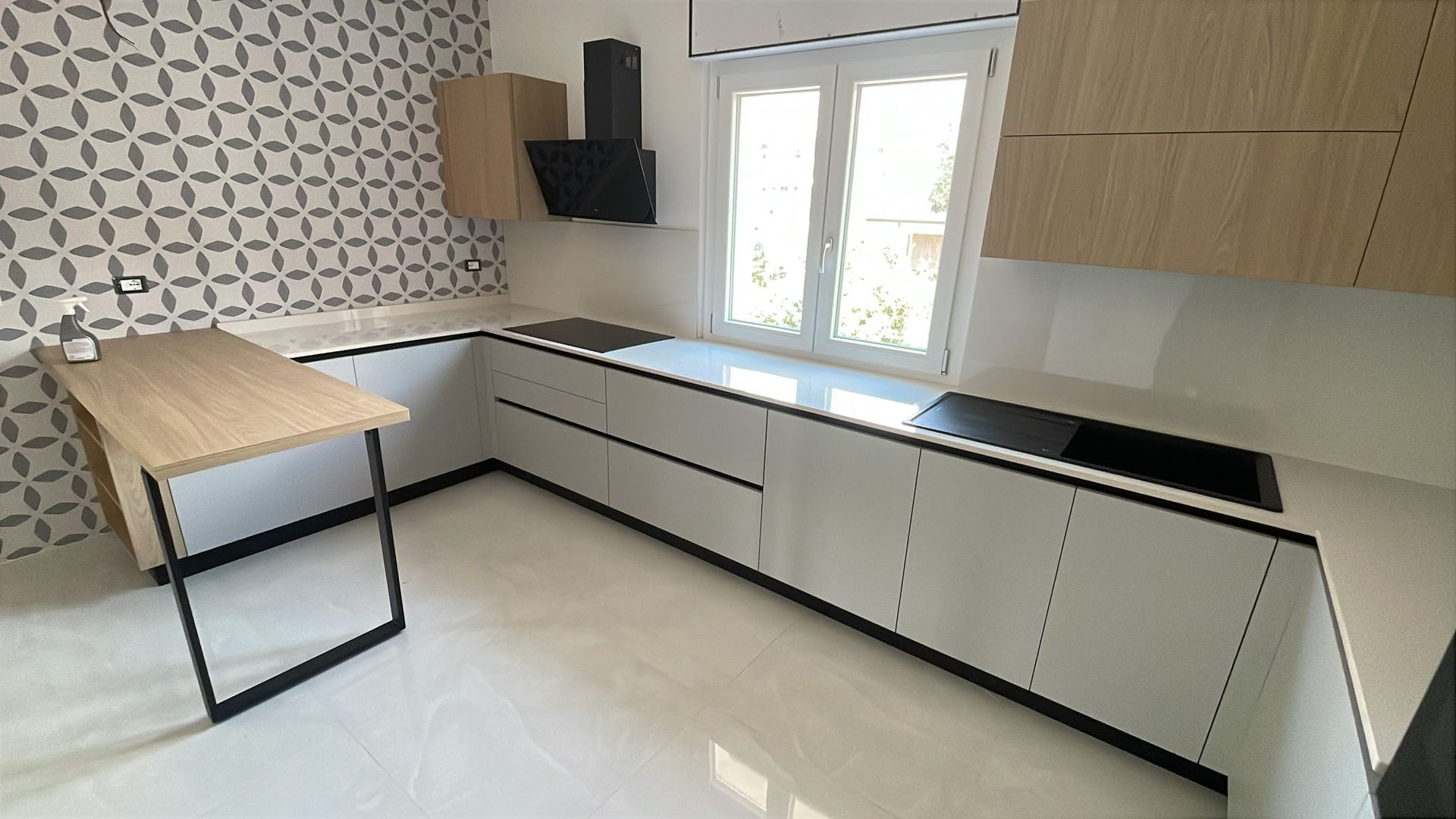 Cucina moderna con mobili bianchi, piani di lavoro neri, paraschizzi decorato e isola in legno.