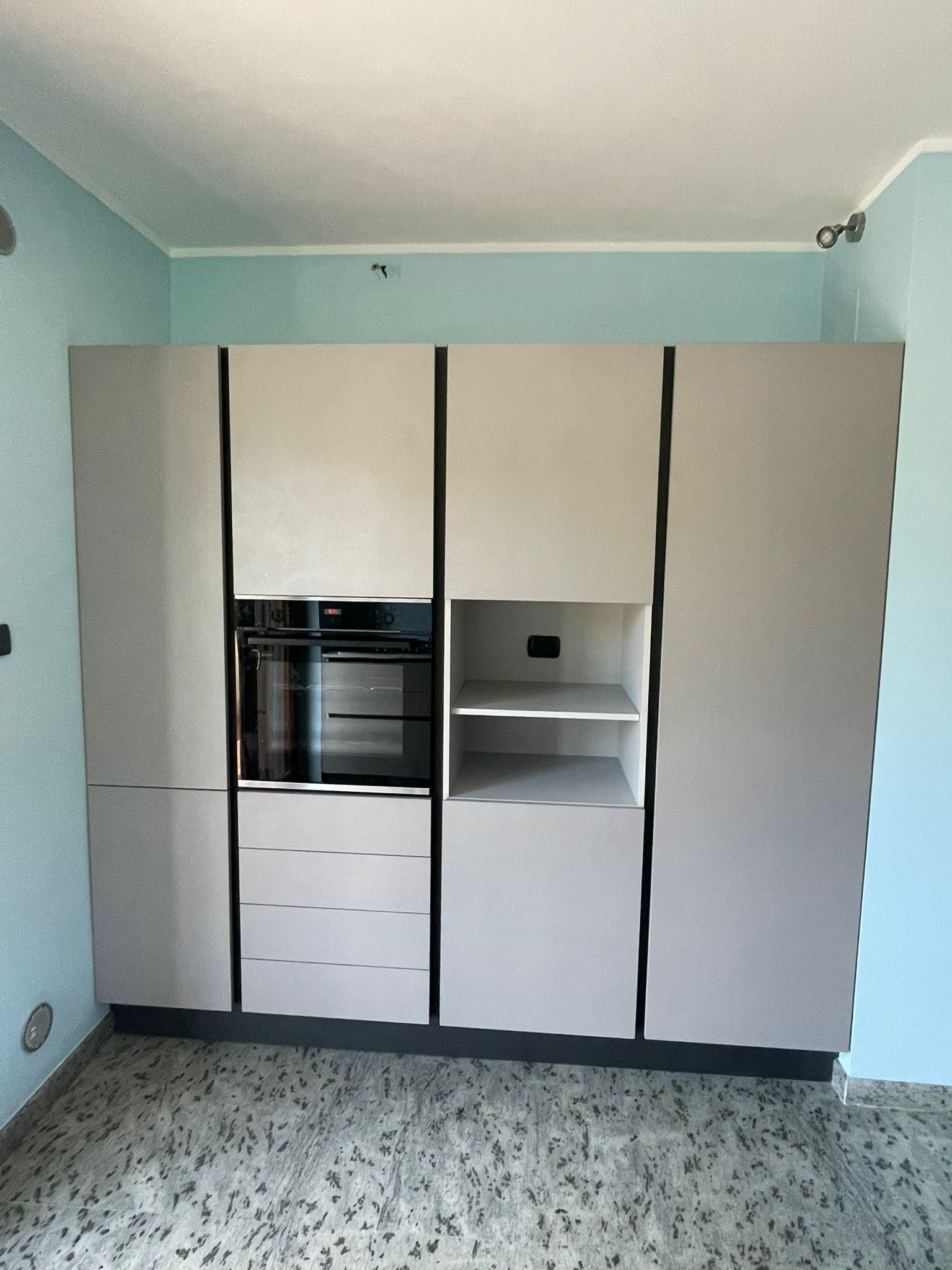 Armadio a muro bianco con finiture nere in una stanza azzurra, con un forno e delle mensole.