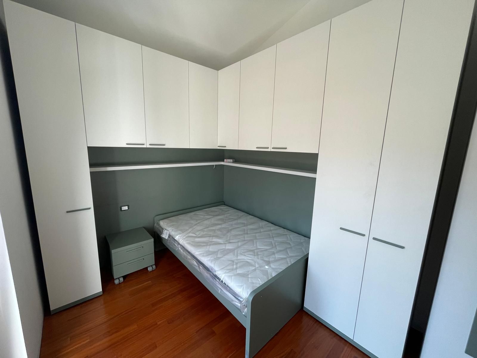 Cameretta con armadi a muro bianchi, un letto singolo e una parete verde con mensole.