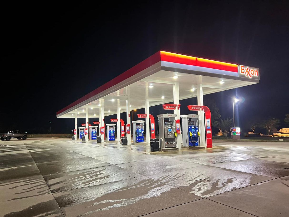 Exxon gas station at night; red and white canopy, illuminated pumps, wet pavement.