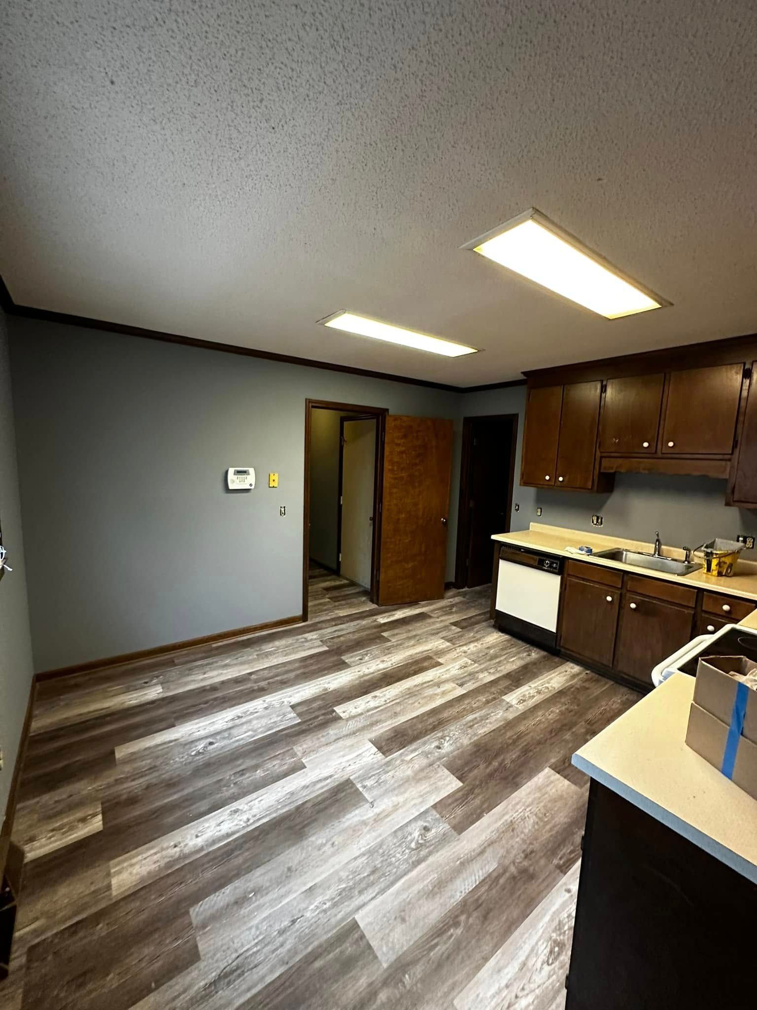Kitchen with gray walls, brown cabinets, and wood-look flooring; doorway to another room.
