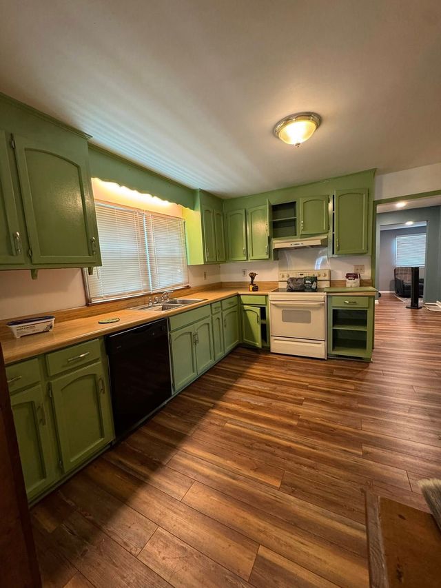 Green kitchen cabinets with a wooden countertop and flooring, white appliances.