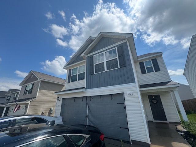 Two-story blue house with white trim, garage, driveway, and parked car under a partly cloudy sky