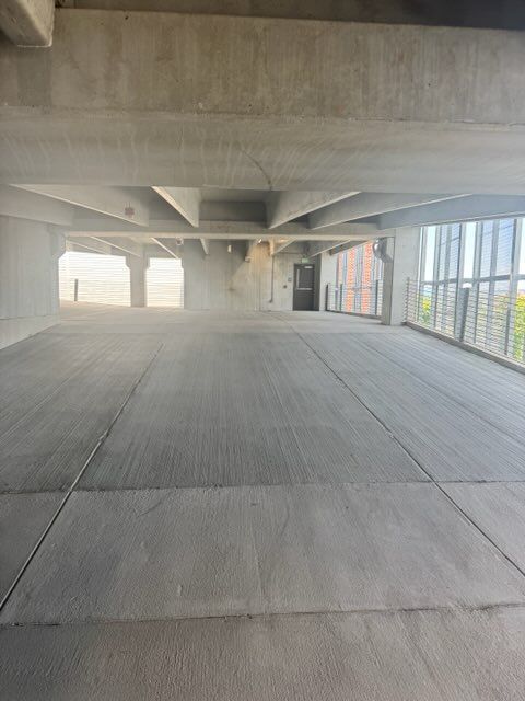 Empty concrete parking garage with pillars, ceiling beams, and daylight from open sides