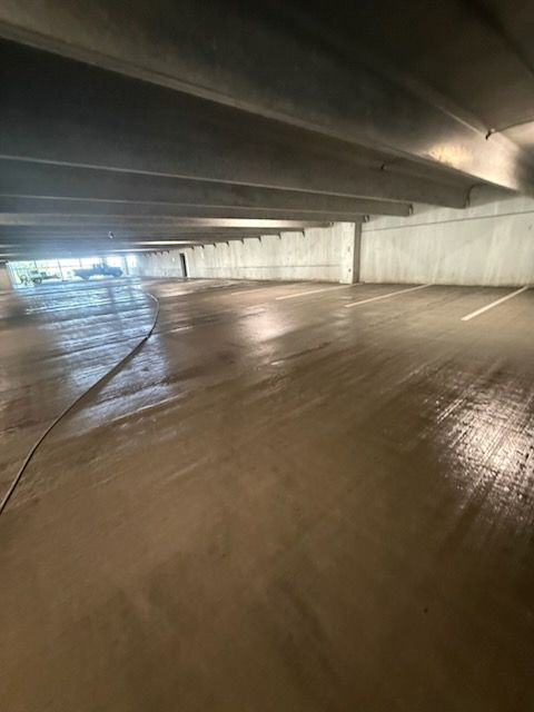 Empty parking garage with wet concrete floor and low ceiling, lit by daylight from the far side