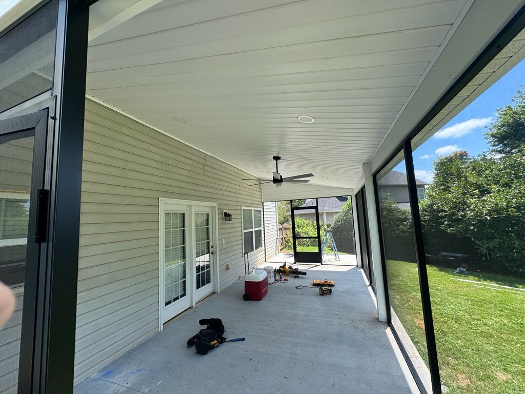 Covered backyard patio with ceiling fan, chairs, and a small dog on the concrete floor