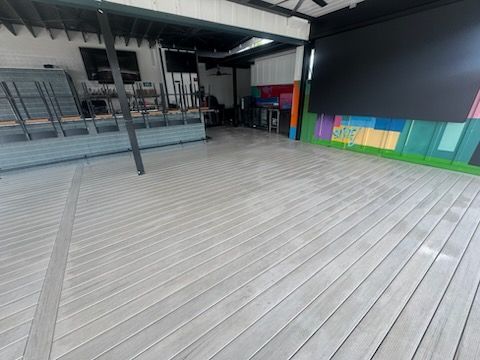 Empty covered outdoor deck with gray wood planks, black beams, and colorful wall panels along the side