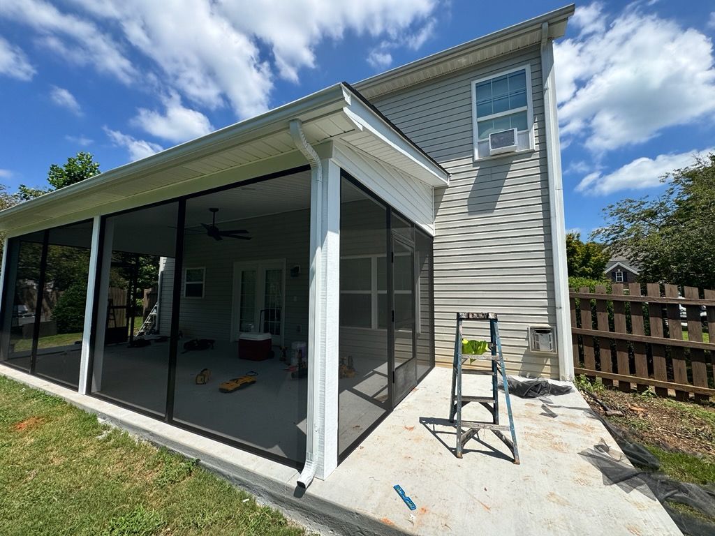Gray house with covered porch, dark roof, and small yard on a cloudy day.