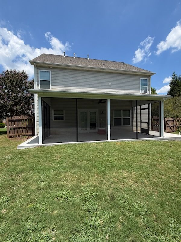 Two-story beige house with a covered back porch and screened patio on a grassy lawn under a blue sky